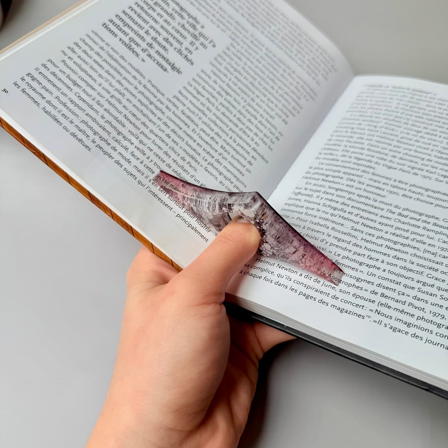Pink and gray resin page holder in geometric shape held by hand during reading.