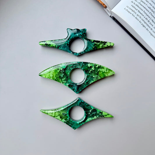 Set of three handmade epoxy resin page holders with abstract green alcohol ink design, shown from top view near an open book.
