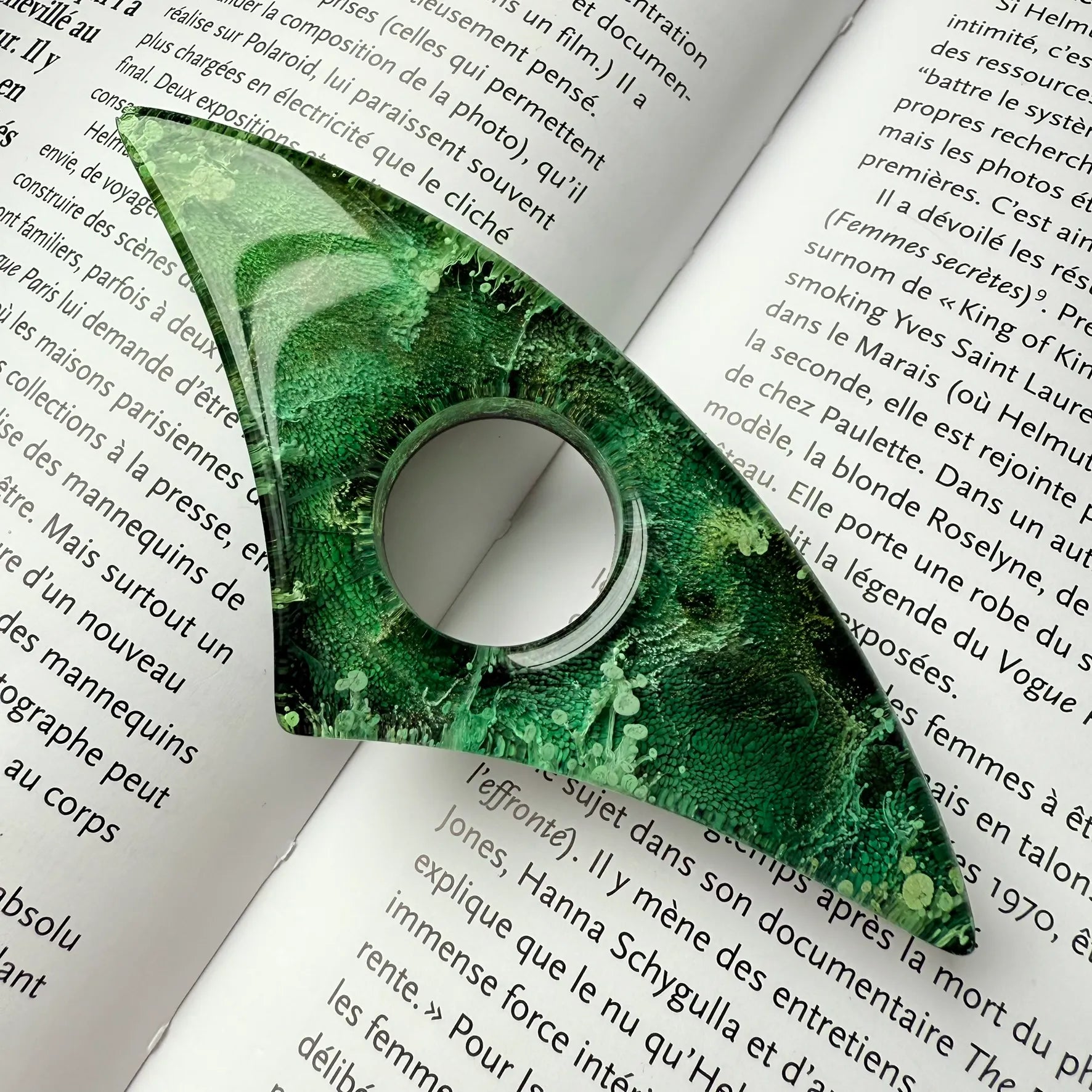 Handmade green resin page holder resting across the center of an open book, showing intricate petri texture and gloss finish.