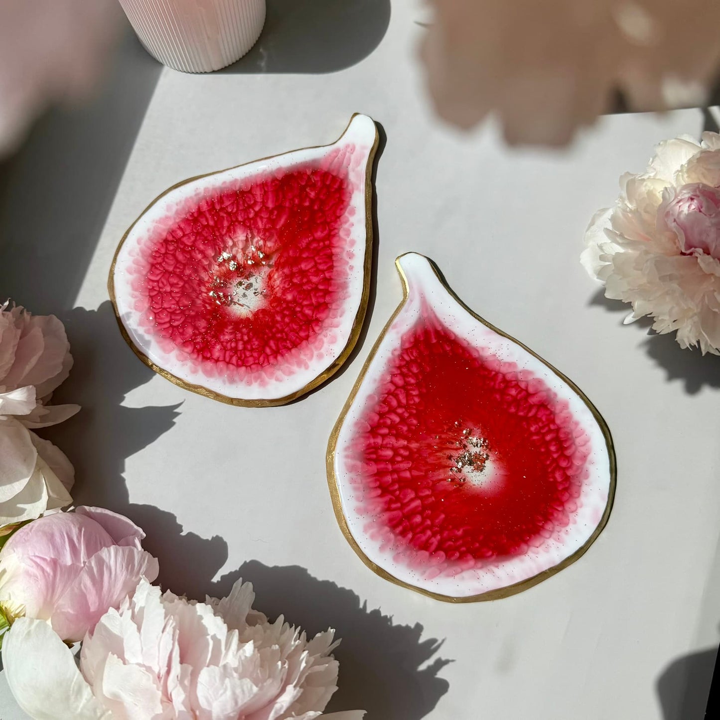 Two sliced fig handmade coaster on a white surface with pink flowers around them