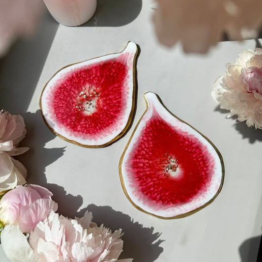 Two sliced fig handmade coaster on a white surface with pink flowers around them
