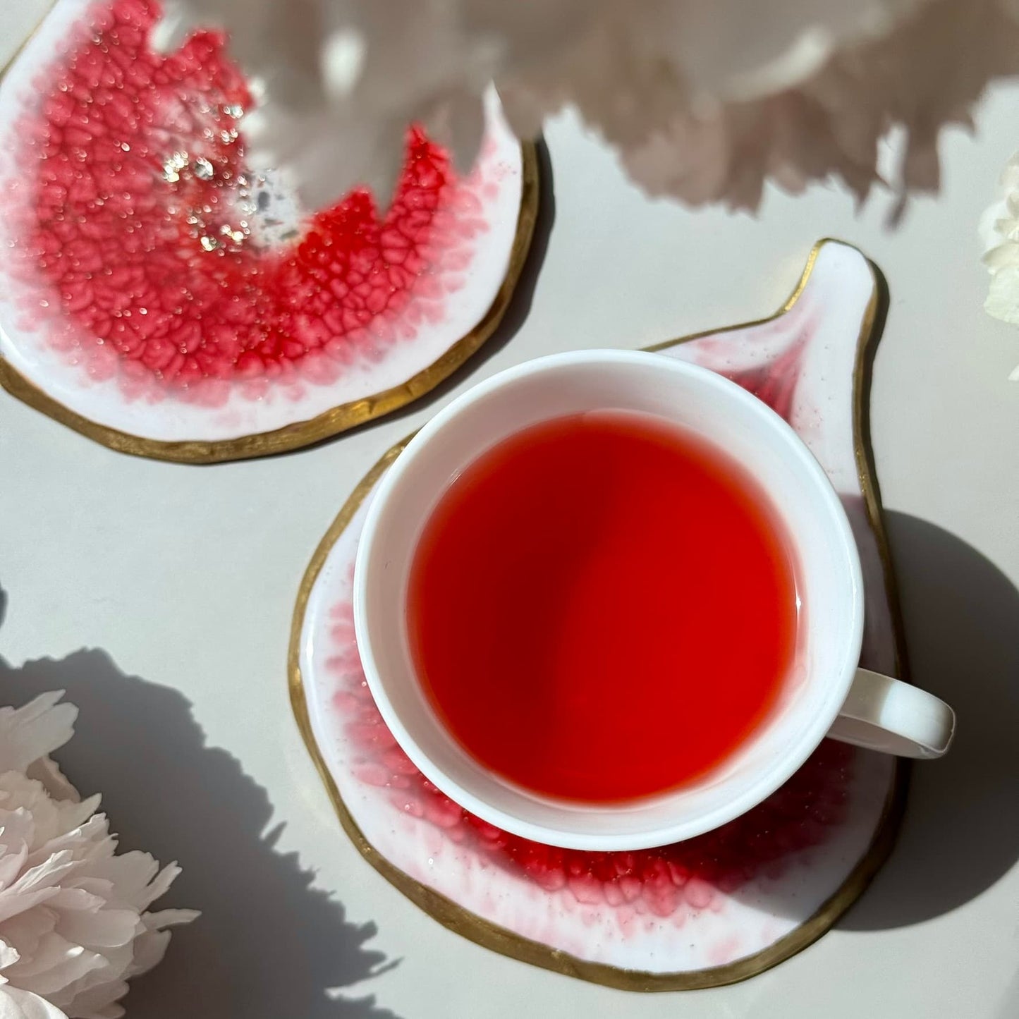 White teacup with tea on a matching saucer, placed on a decorative handmade fig-shaped coaster with floral patterns