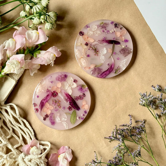Two round, floral-patterned coasters on a brown surface with flowers around them.