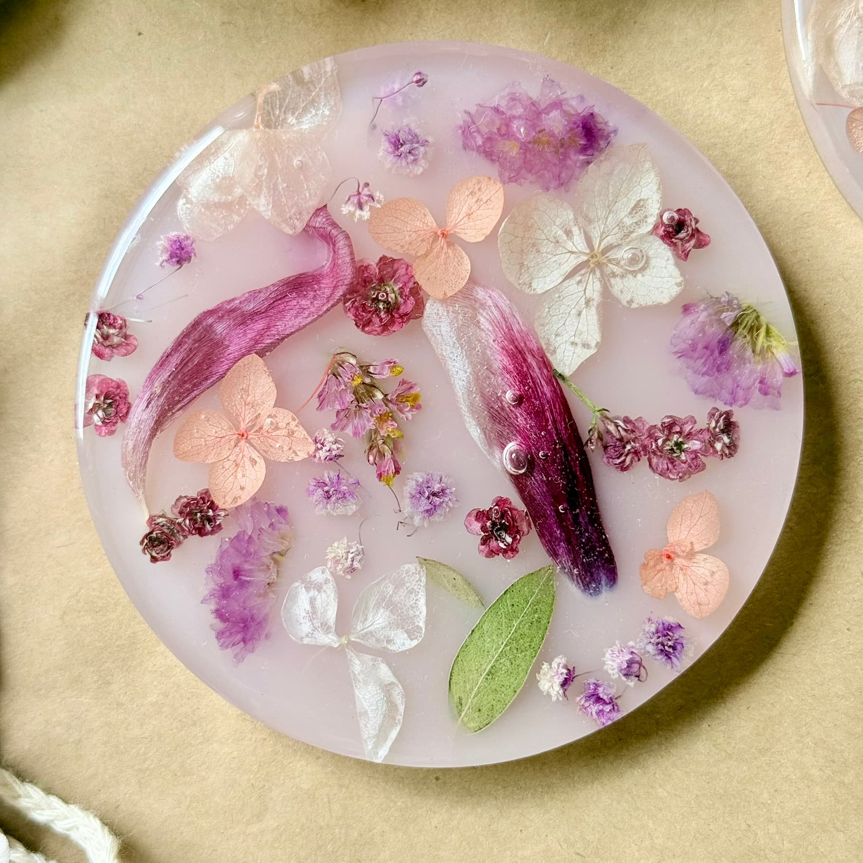 Handmade round coaster with pink and purple flowers, butterflies, and leaves on a beige background