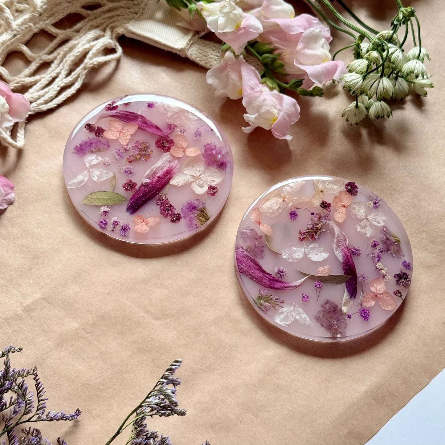 Two round resin coasters with floral designs on a brown surface with flowers around.