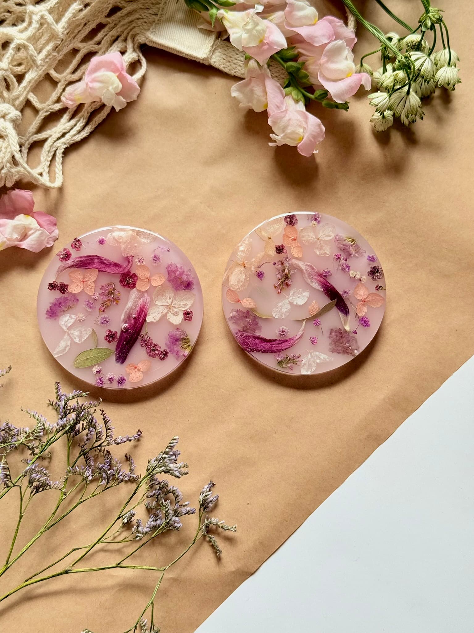 Two round pink resin coasters with floral embedded design on a brown surface with flowers and twine.