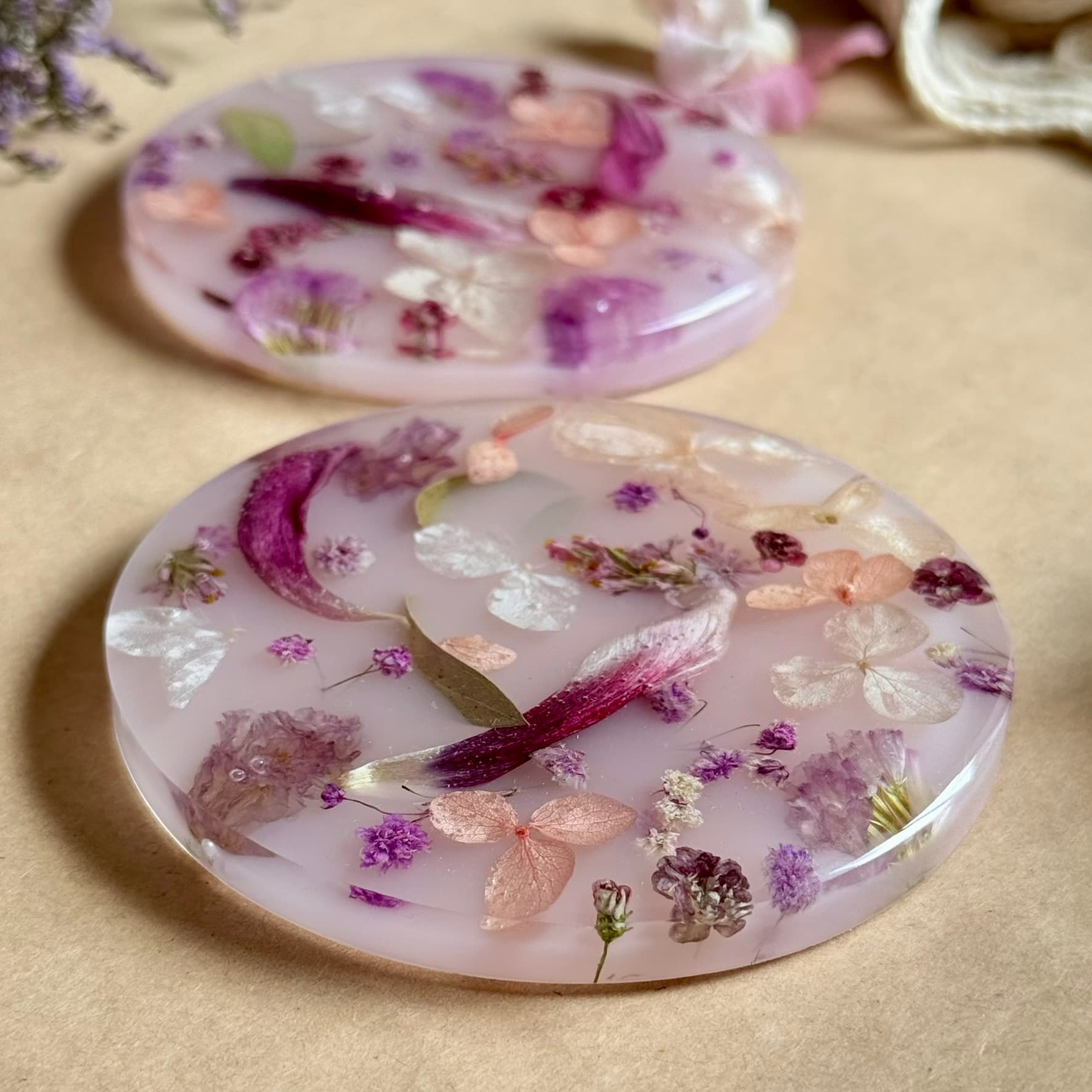 Round resin coasters with pressed flowers on a beige surface
