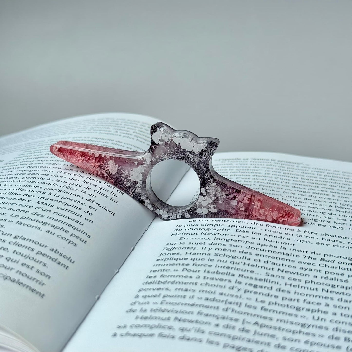 handmade resin page holder in pink and smoky gray tones, propping open a book.