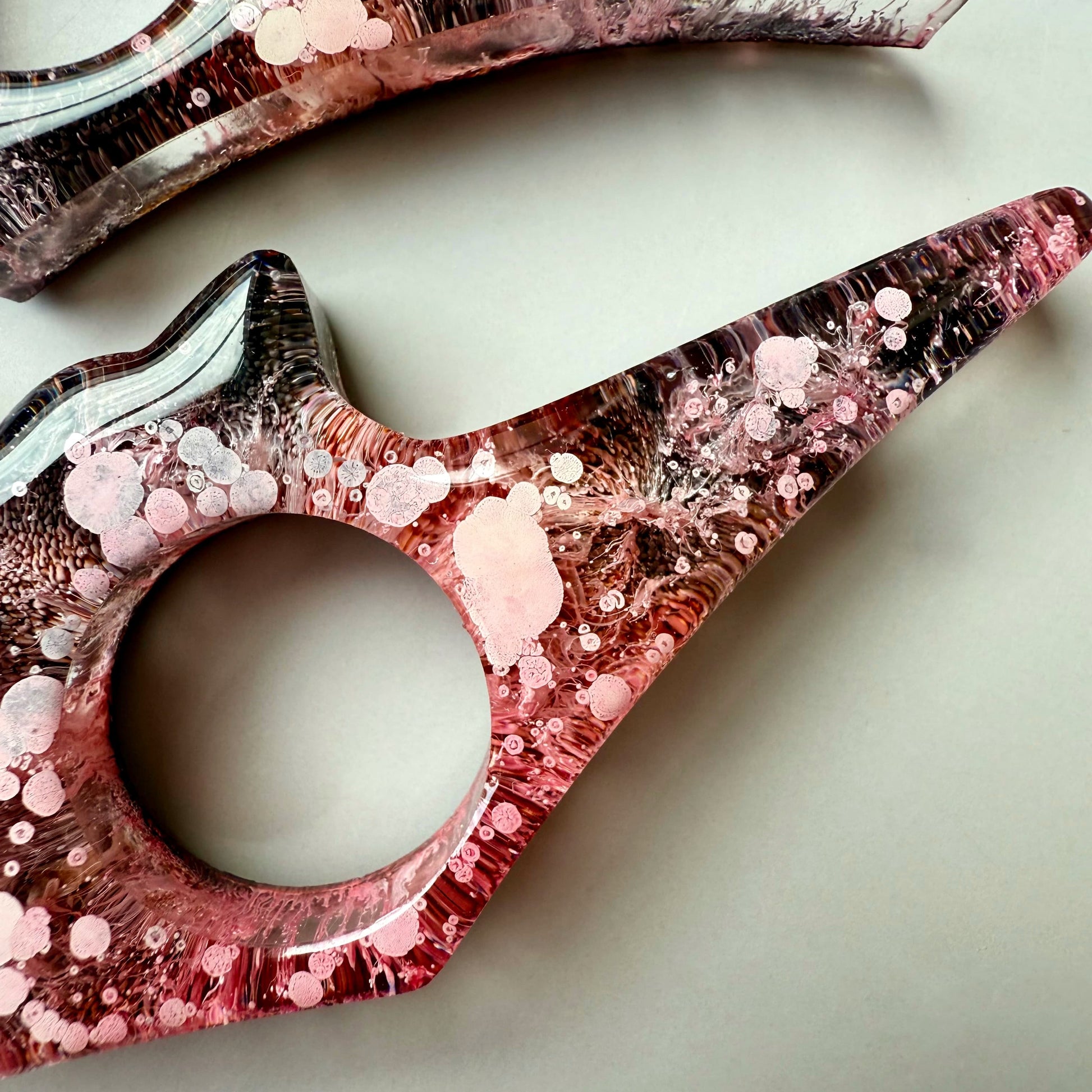Close-up of cat-shaped resin page holder with pink alcohol ink texture and layered petri effect.