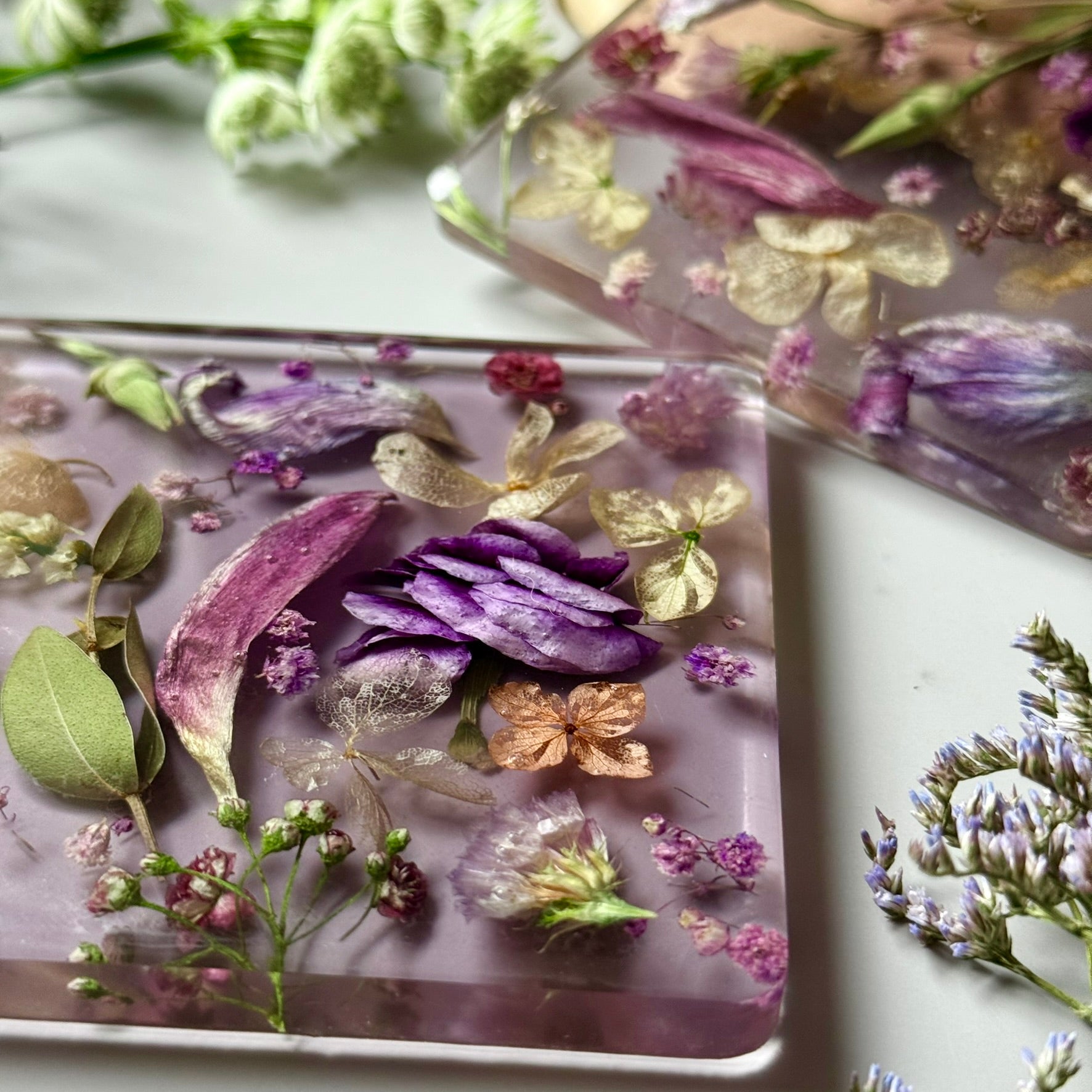 Detailed view of dried purple flowers and golden leaves embedded in resin, capturing the handmade texture and elegance.