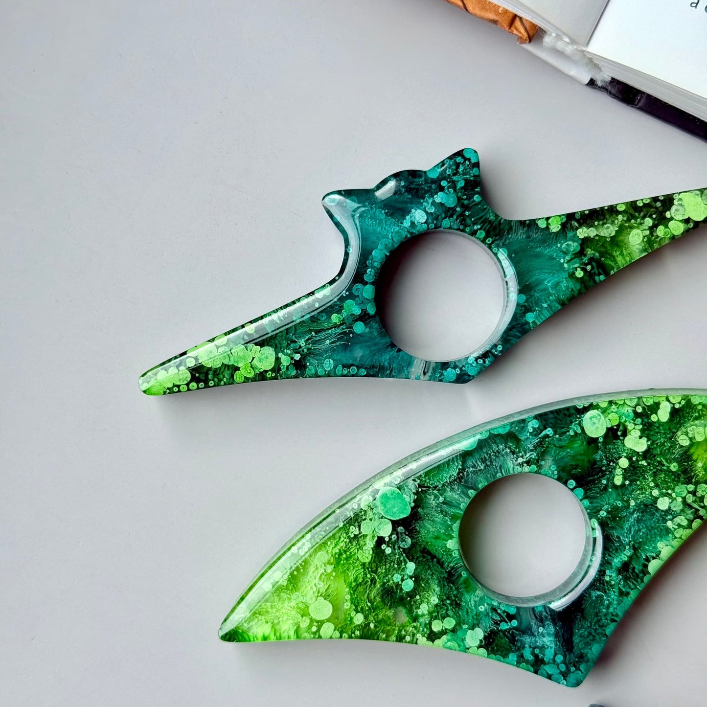 Close-up of handmade green resin page holders with unique petri ink patterns and botanical details.