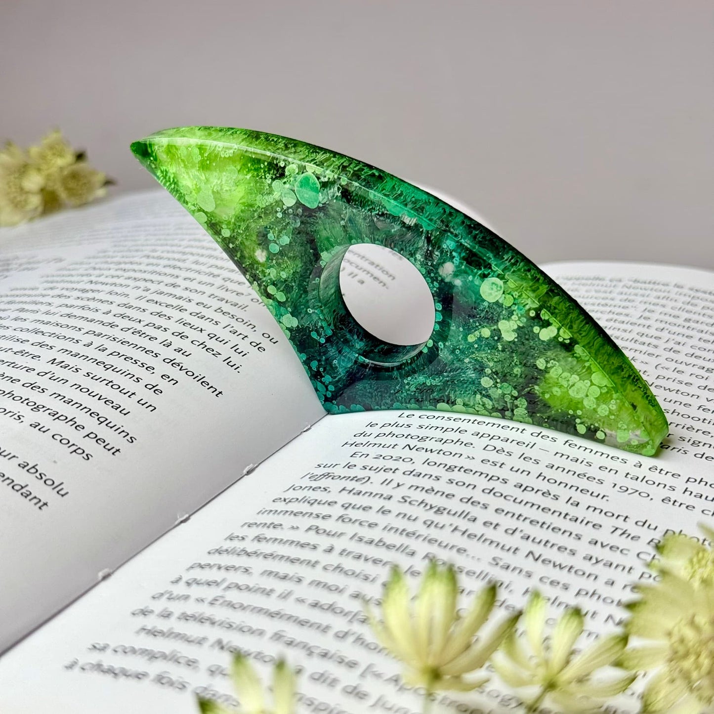 Curved handmade resin page holder in green and teal alcohol ink art, propping open a book for hands-free reading.