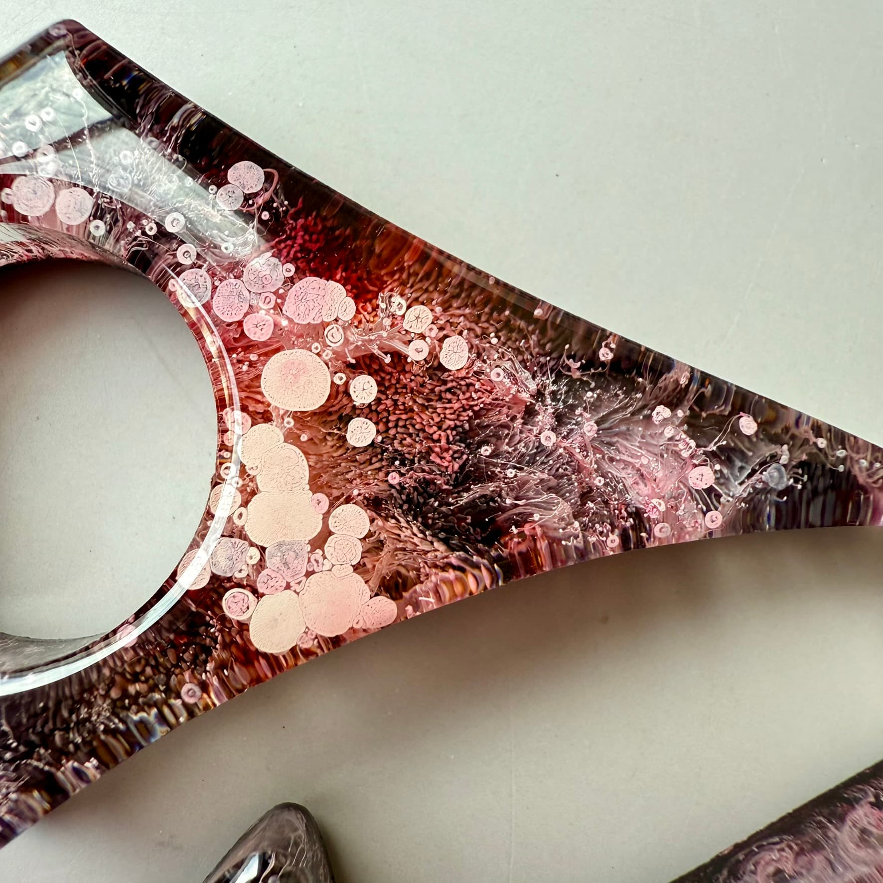 Detailed view of red and pink handmade resin page holder with blooming petri ink texture and layered pigment depth.