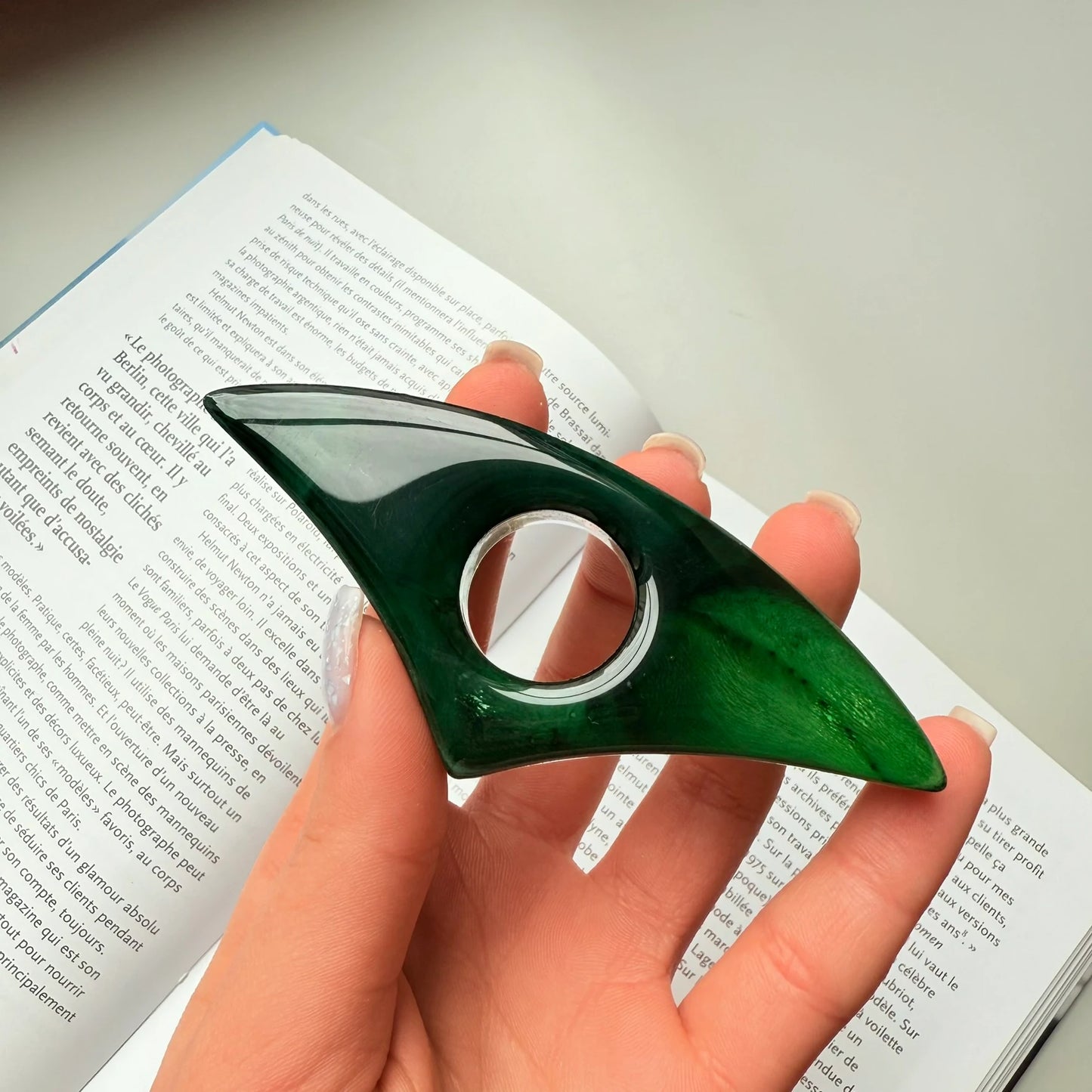 Dark emerald green handmade resin page holder held in hand above an open book.