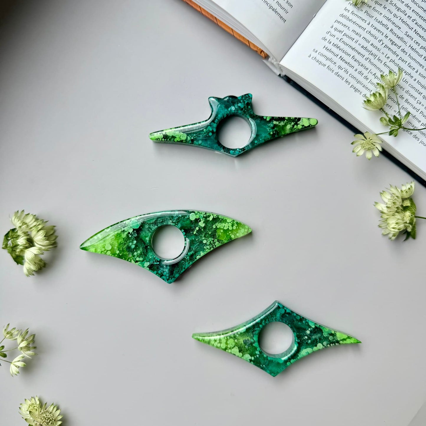 Green and teal petri resin art page holders laid out flat, styled for product photography near a book.