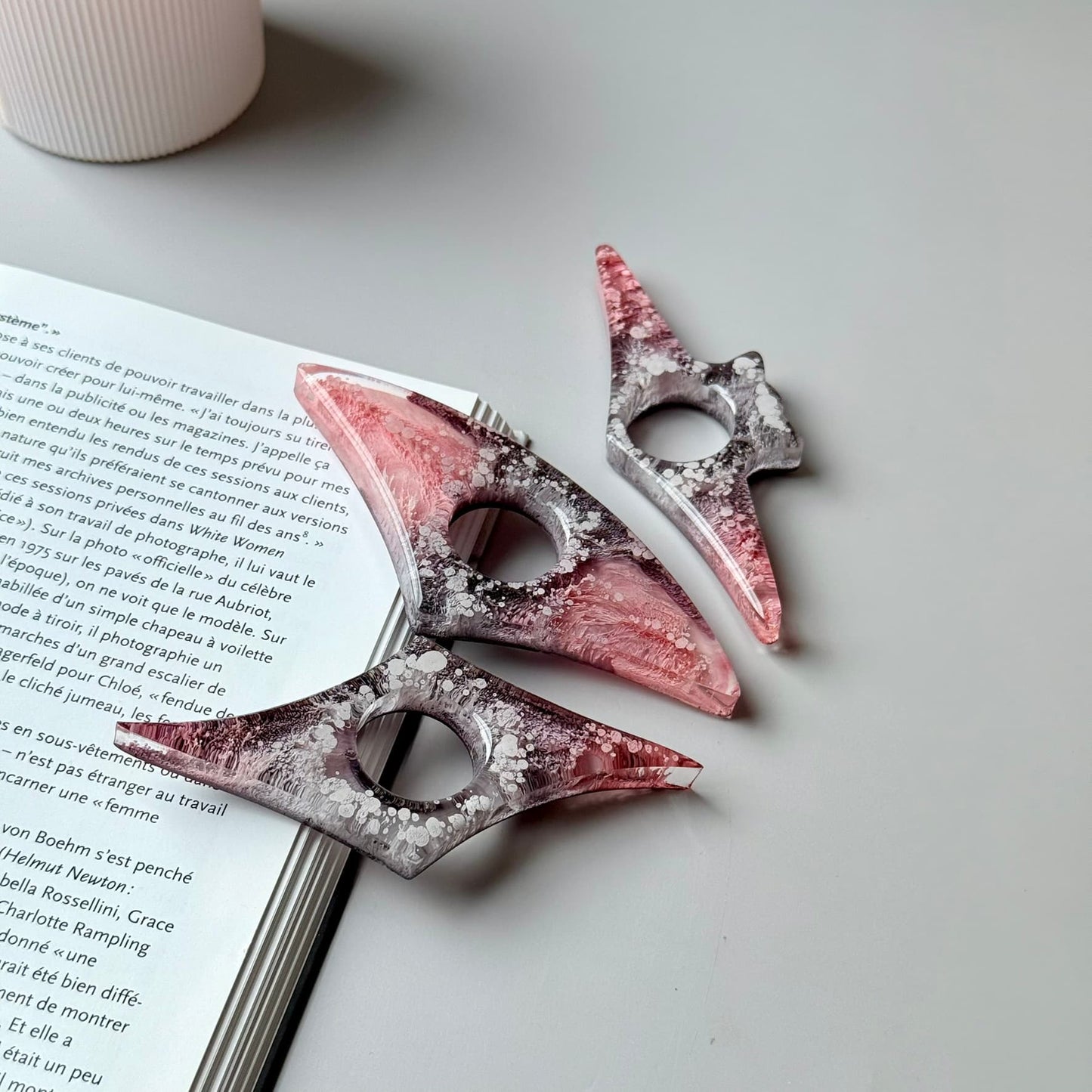 Handmade resin page holders in pink-gray color palette arranged next to an open book.