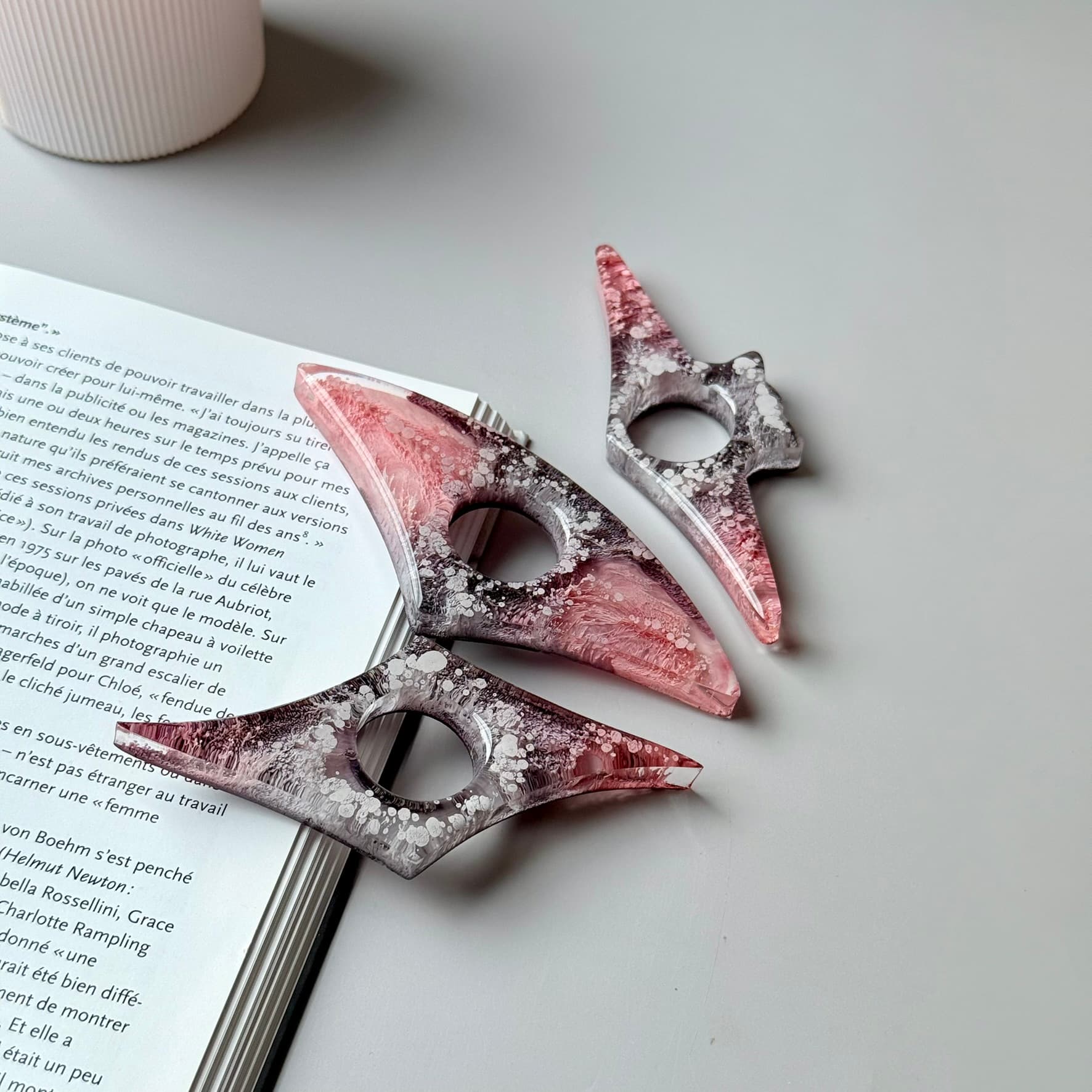 Handmade resin page holders in pink-gray color palette arranged next to an open book.