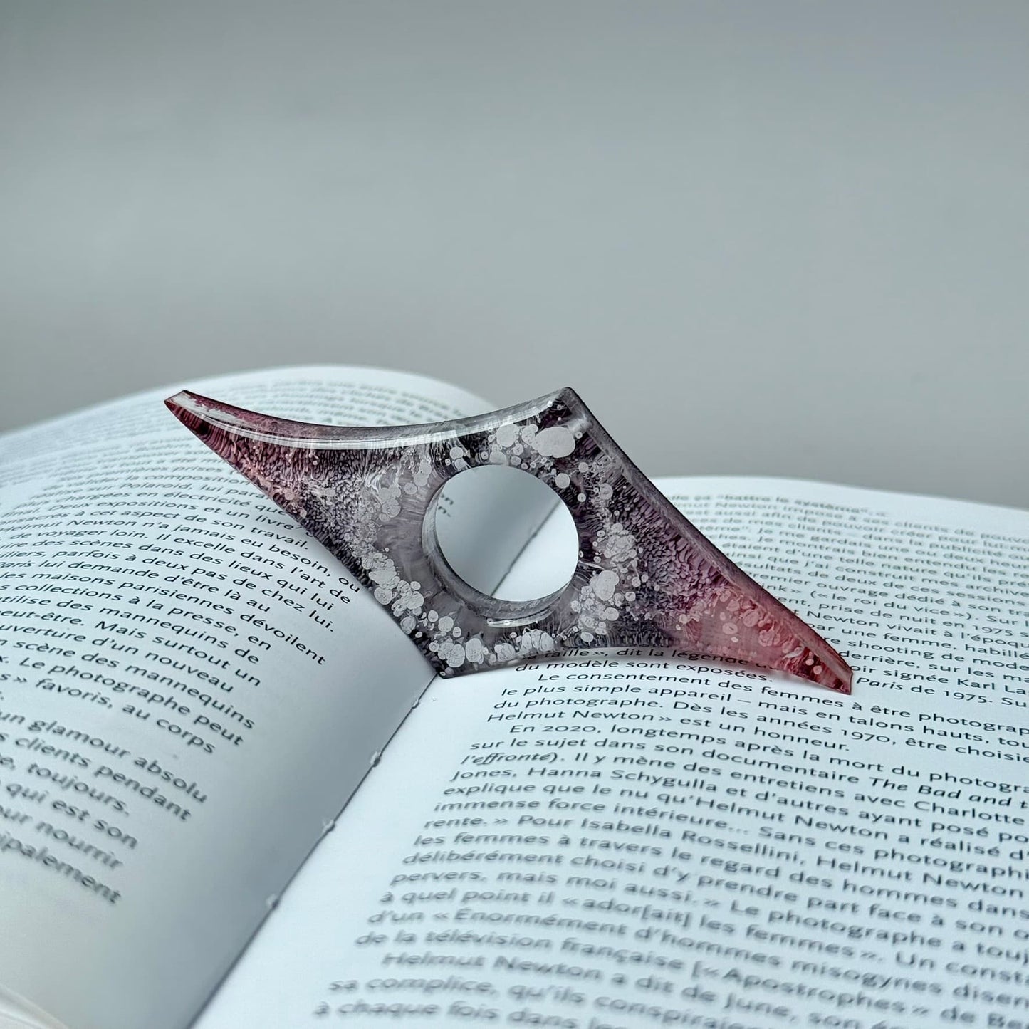 Geometric handmade resin page holder in pale pink and gray alcohol ink art, holding a book open.