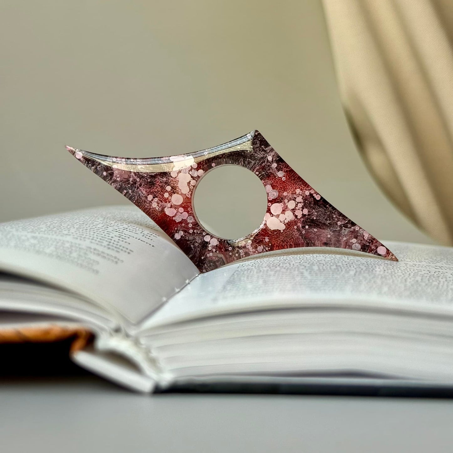 Geometric handmade resin page holder in deep red and pink tones, placed across the open pages of a book.