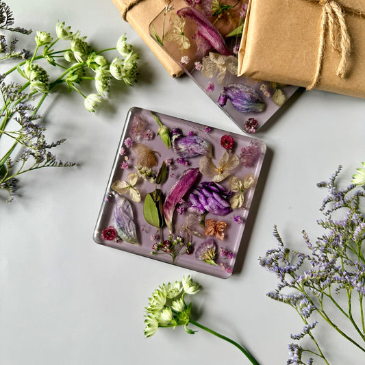 Set of resin coasters with pressed flowers, wrapped as a gift with natural twine and surrounded by delicate greenery.