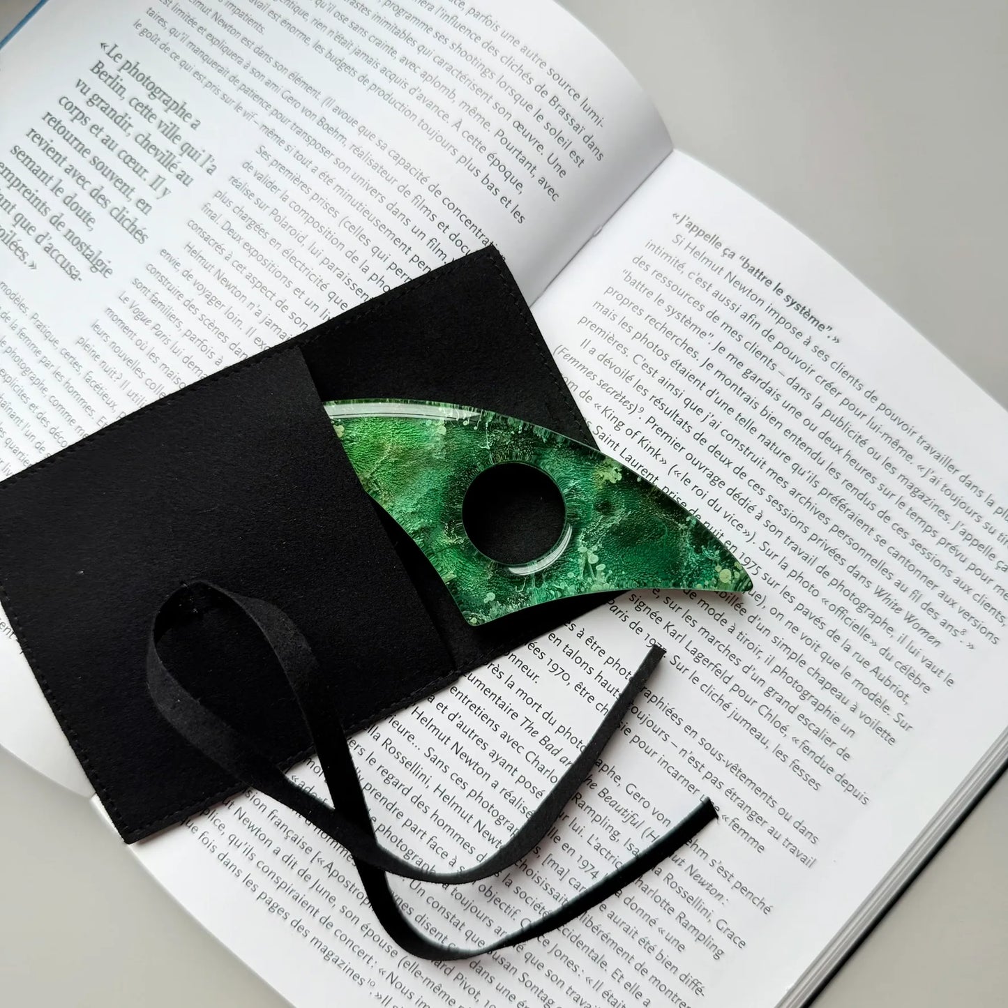 Handmade green resin page holder partially tucked inside black gift pouch on top of an open book.