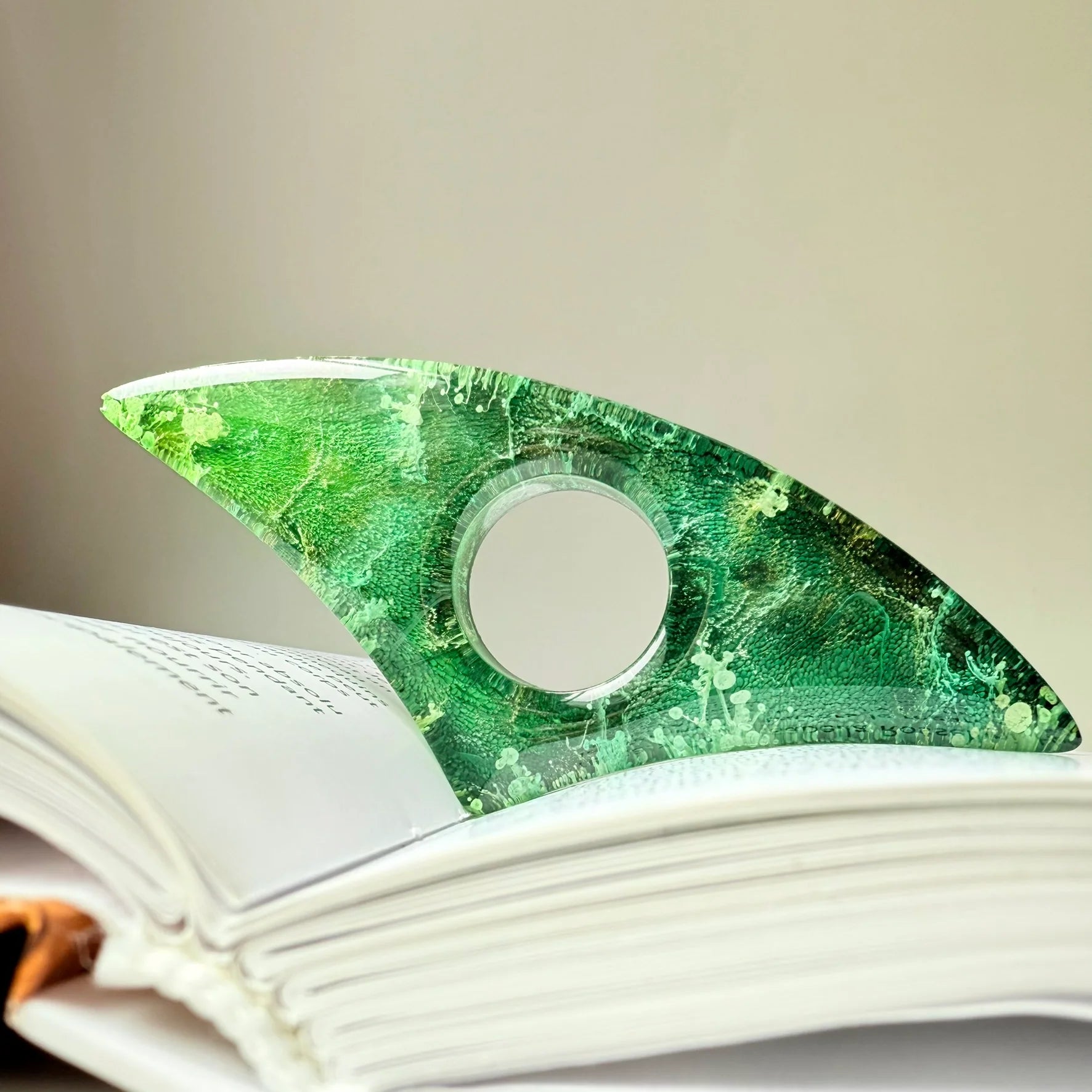 Curved handmade resin page holder in vivid green tones with botanical petri effect, propping open a white book.