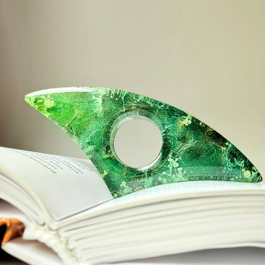 Curved handmade resin page holder in vivid green tones with botanical petri effect, propping open a white book.