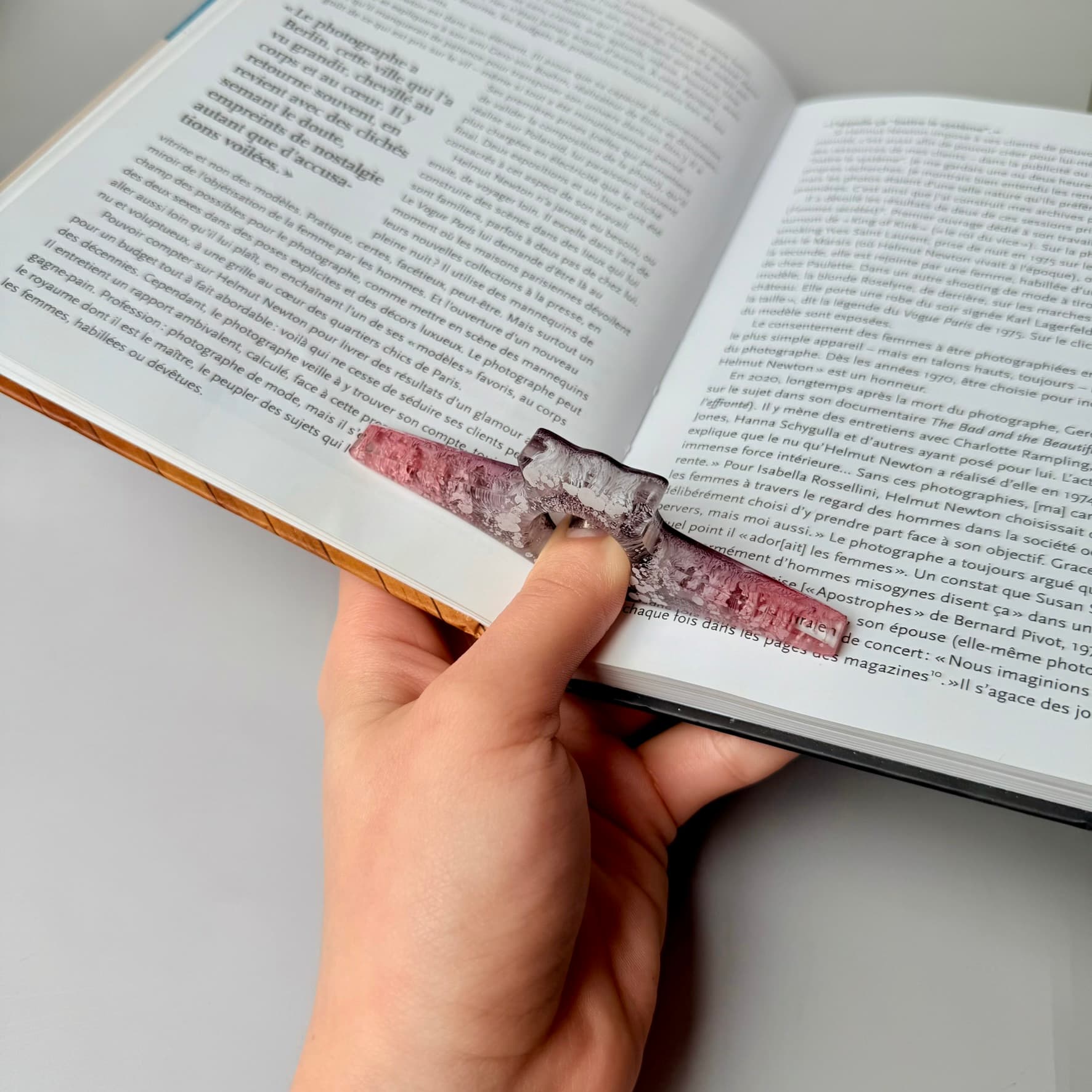 Hand using a pink and gray resin page holder to keep book open.