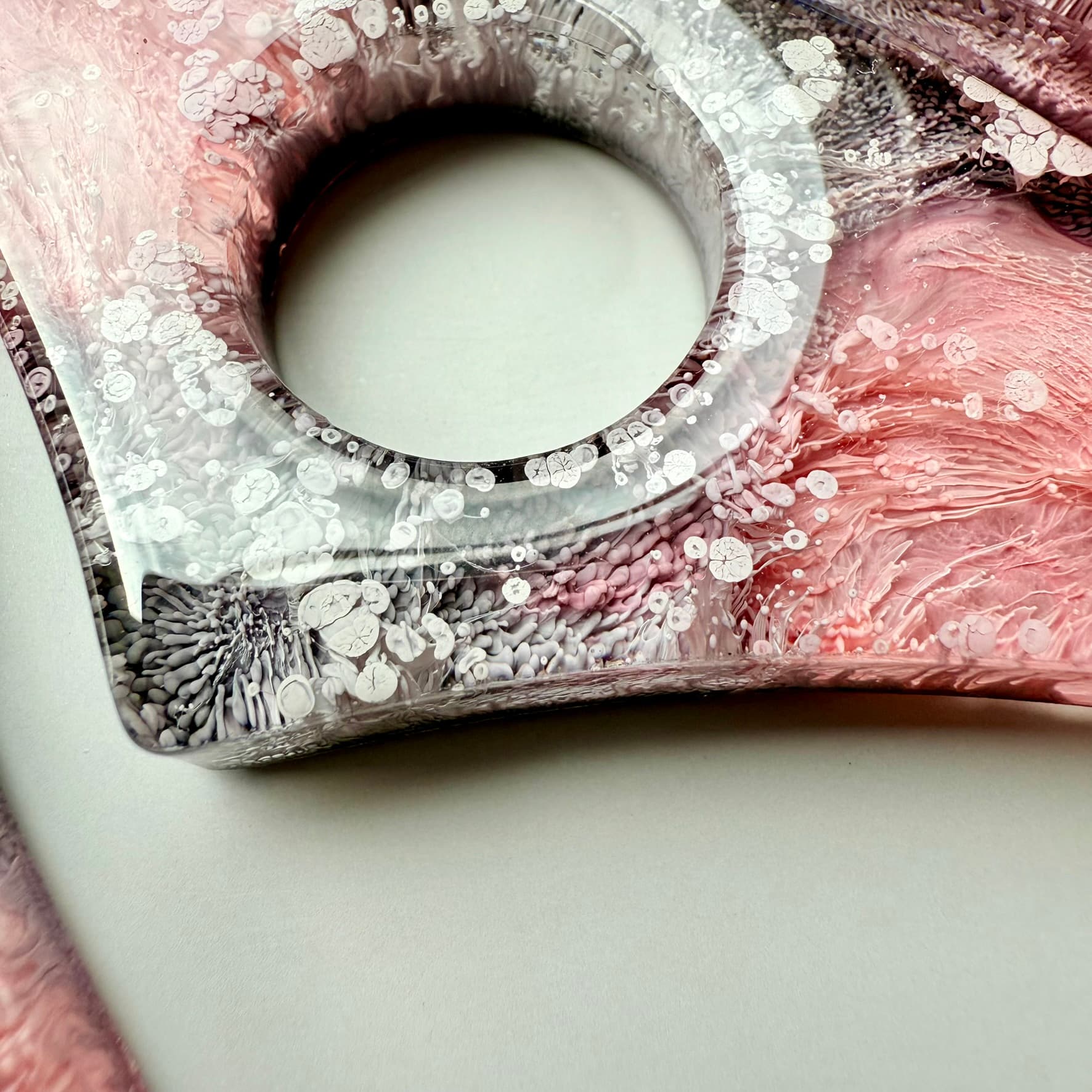 Detailed macro of resin page holder with white petri ink bubbles and pink-gray swirls.