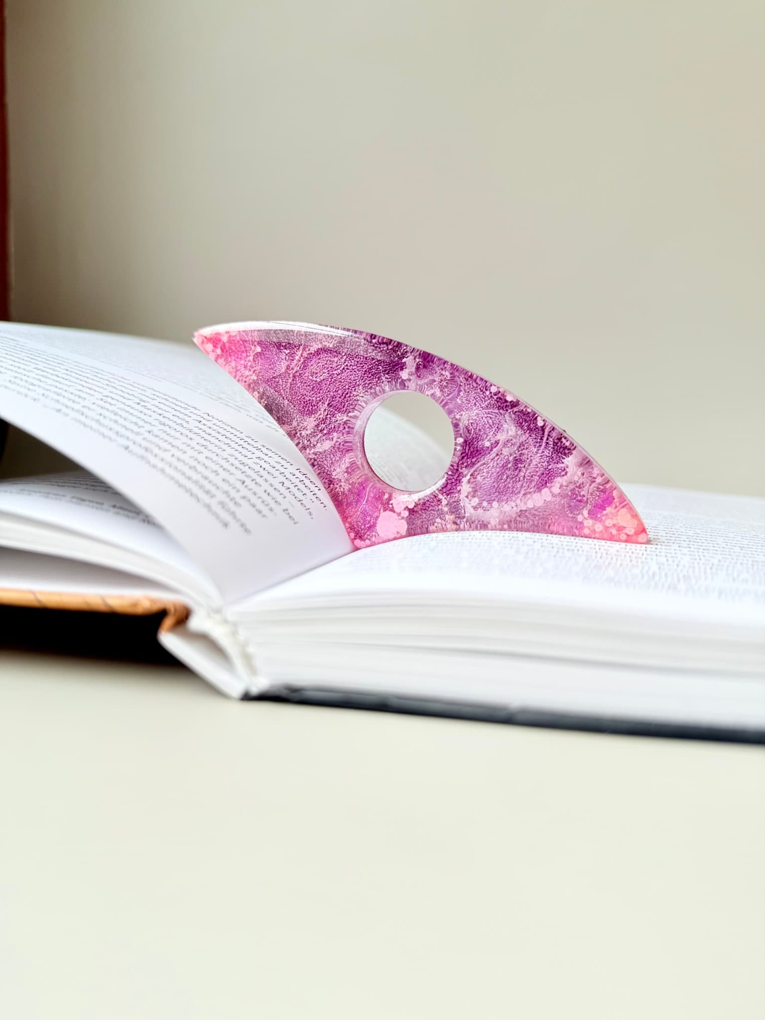 Pink and white marbled handmade page holder on an open book with a plain background