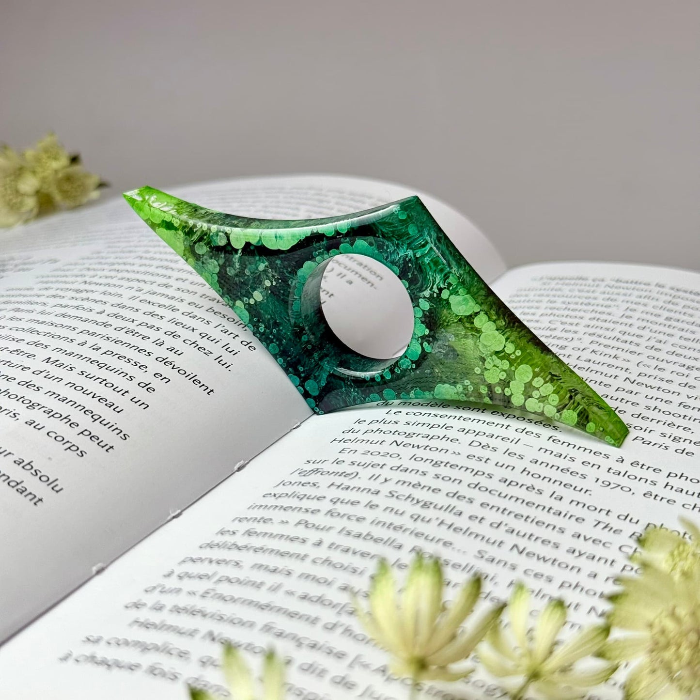 Handmade resin page holder with pointed edges and green ink swirl design, holding a book open mid-read.
