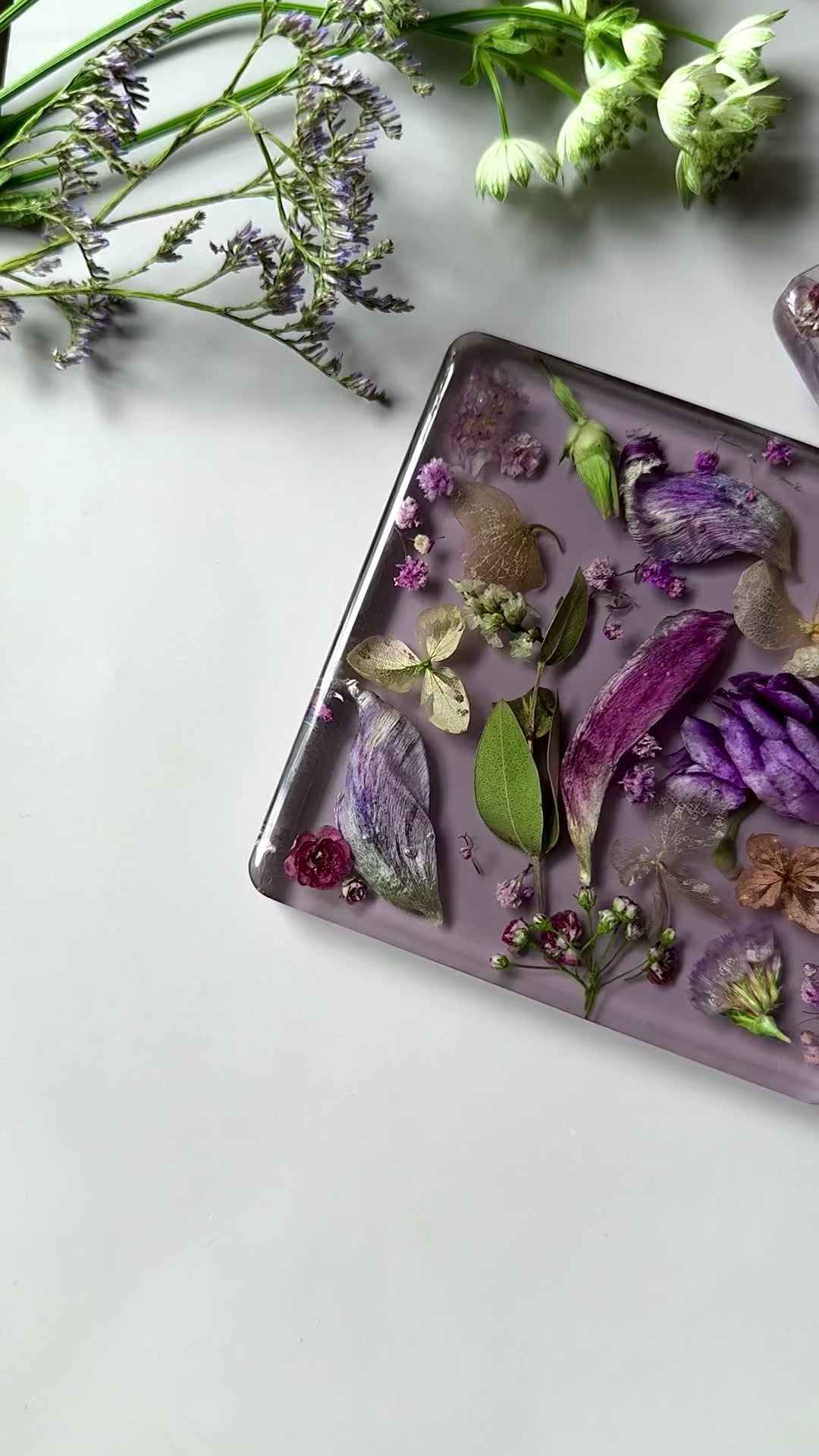 Handmade square resin coasters with real dried flowers in purple and gold tones on a soft lavender background.