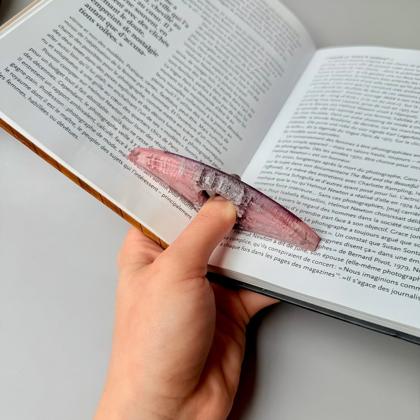 Reader using handmade pink resin page holder to hold open a book, side view.