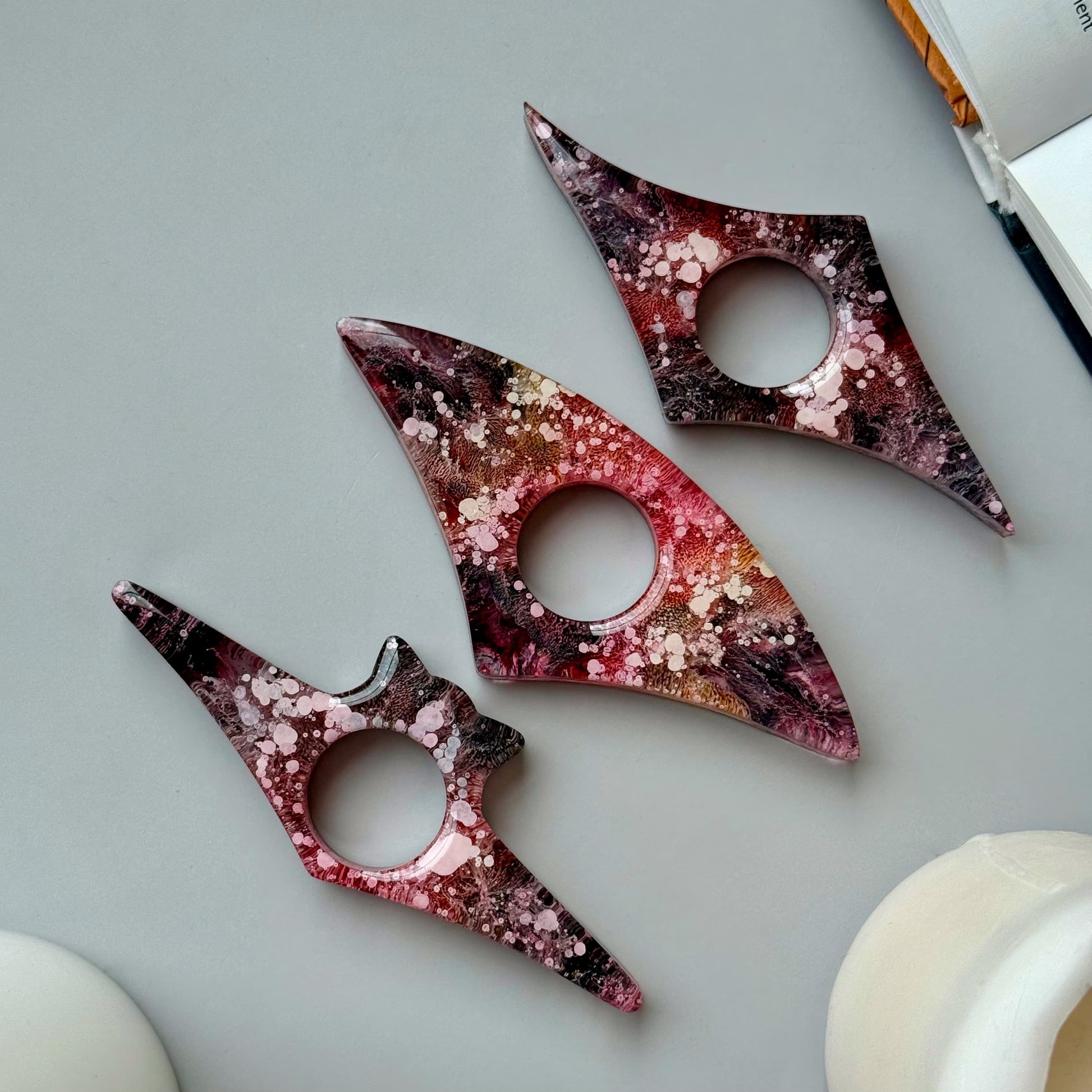 Handmade resin page holders in red, pink, and black petri design, styled flat with abstract shapes and a neutral background.