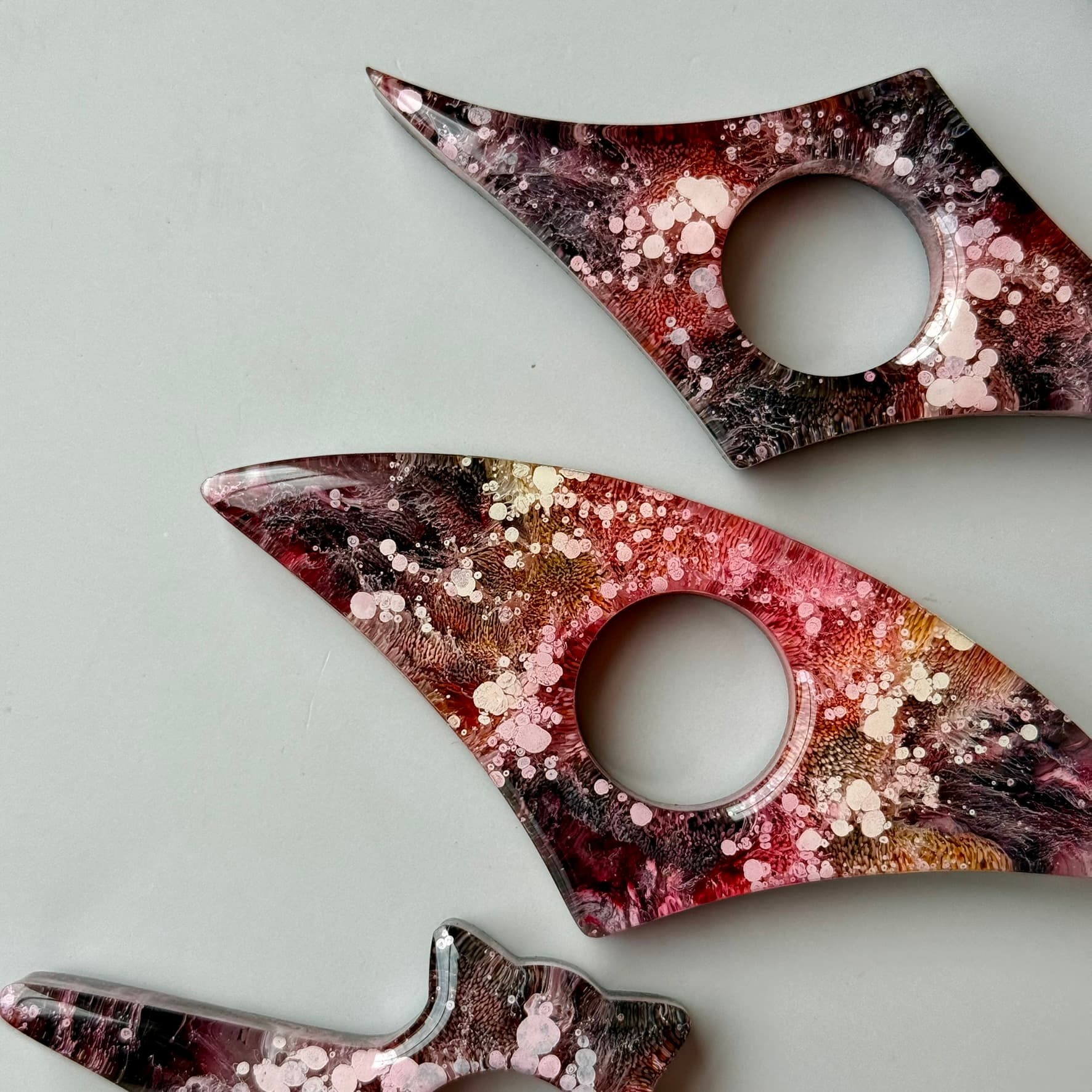 Three handmade resin page holders in red, pink, and black petri design arranged flat with abstract shapes on neutral background.