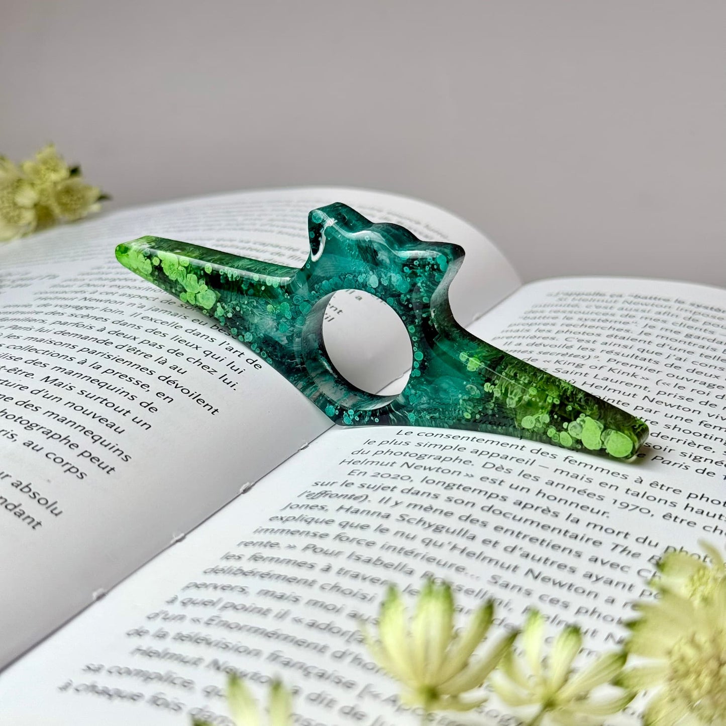 Green cat-shaped handmade resin page holder resting on an open book, showing its use for reading.