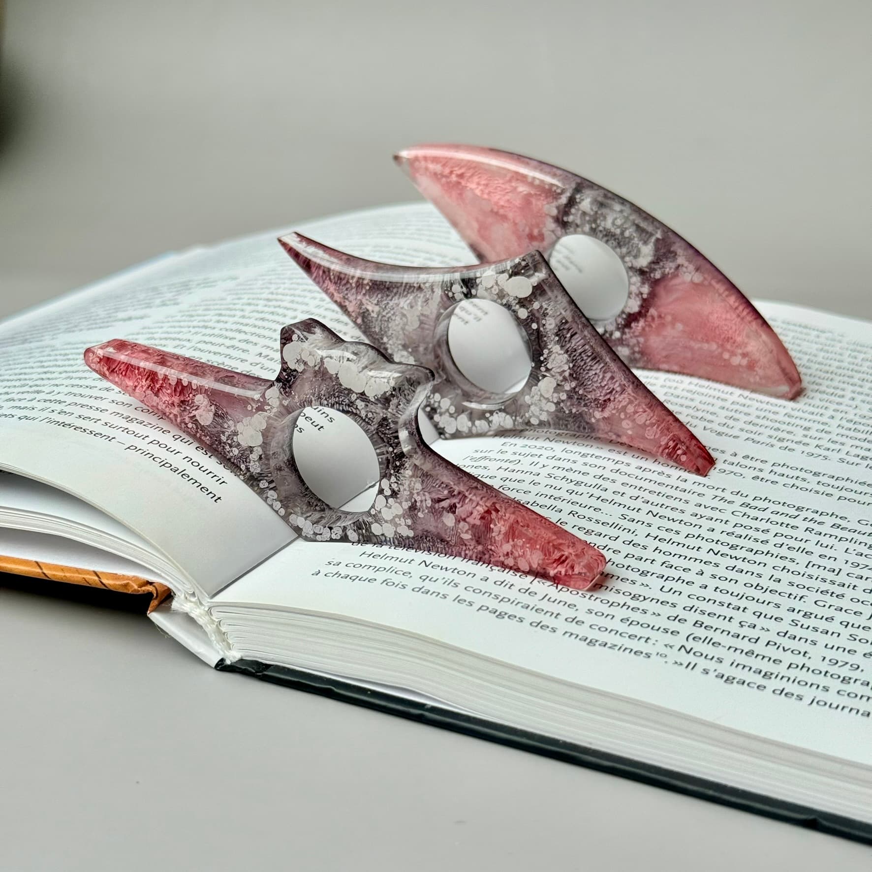 Trio of handmade resin page holders in pink and gray petri effect, styled on open book.