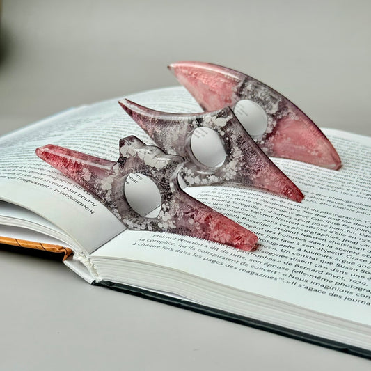 Trio of handmade resin page holders in pink and gray petri effect, styled on open book.