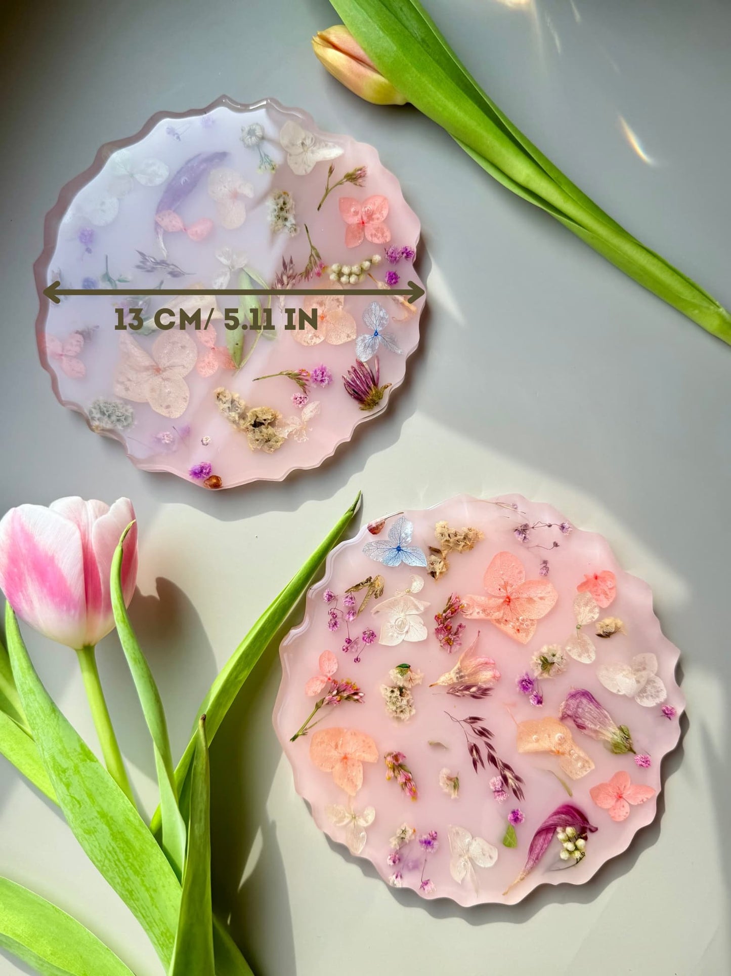 Decorative handmade pink coasters with floral designs on a gray surface with tulips.