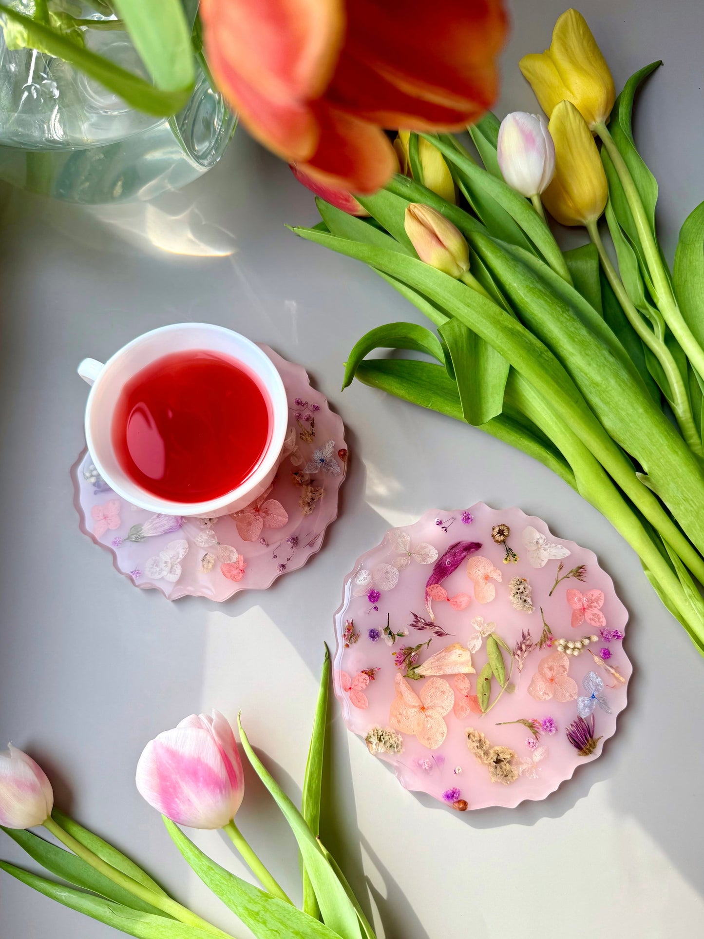 Teacup with red liquid, floral handmade coasters, and tulips on a light surface
