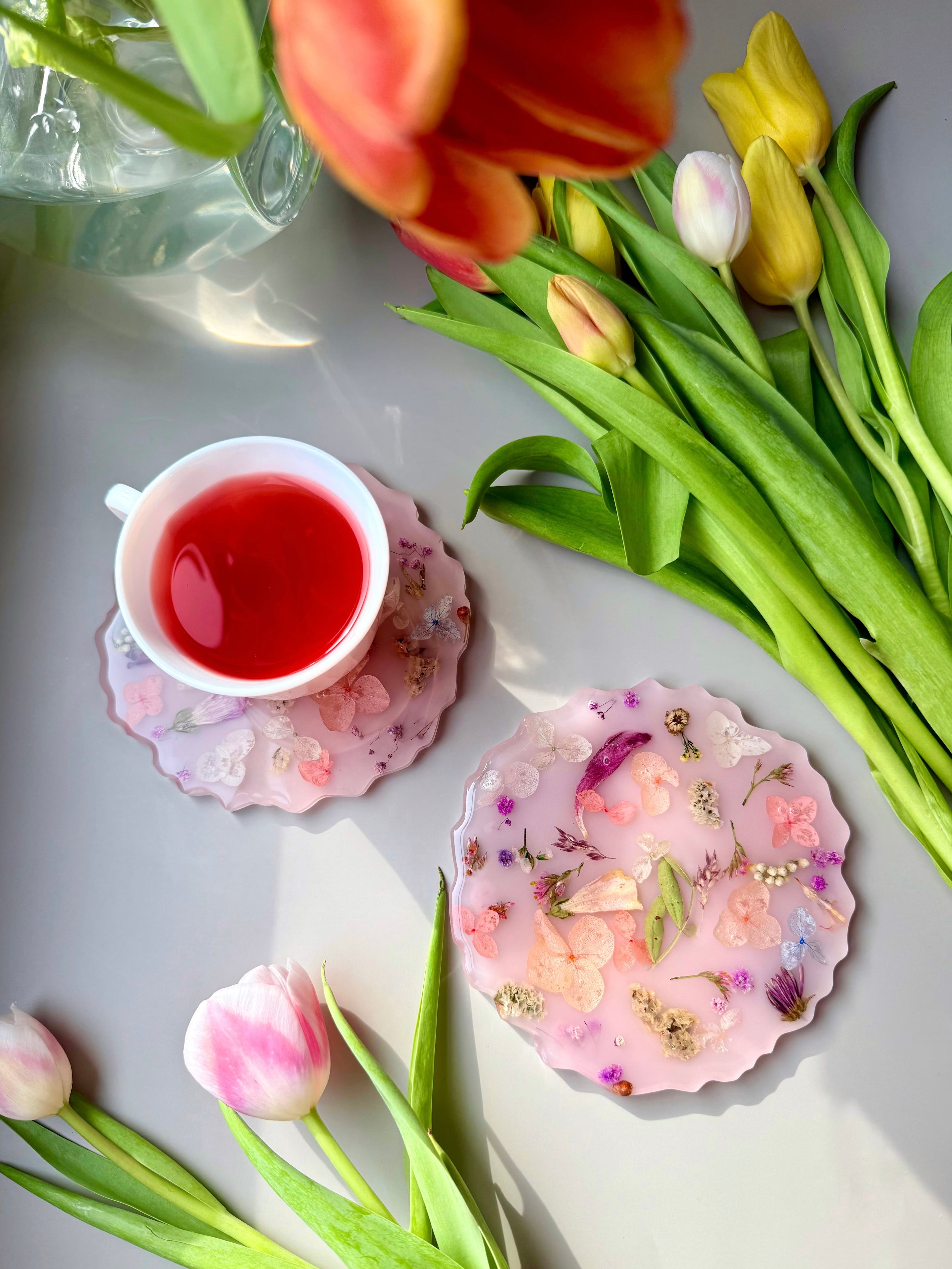 Teacup with red liquid, floral handmade coasters, and tulips on a light surface